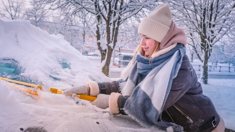 Vrouw maakt auto sneeuwvrij voor een veilige autorit